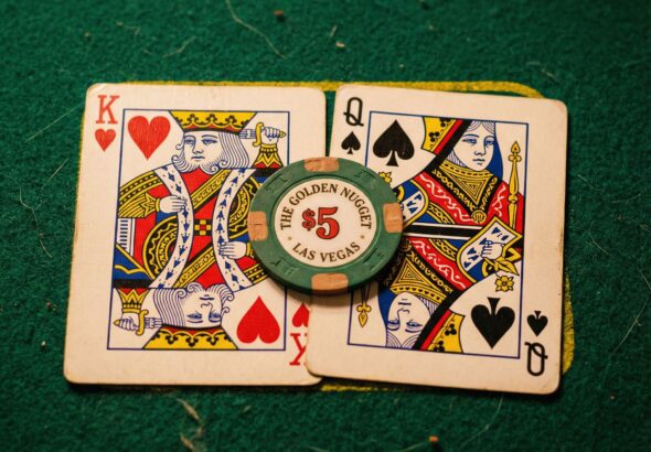 초록색 펠트 카지노 테이블 위에 나란히 놓인 킹과 퀸 카드, 그 위에 포커 칩 하나가 얹혀 있는 모습이다.