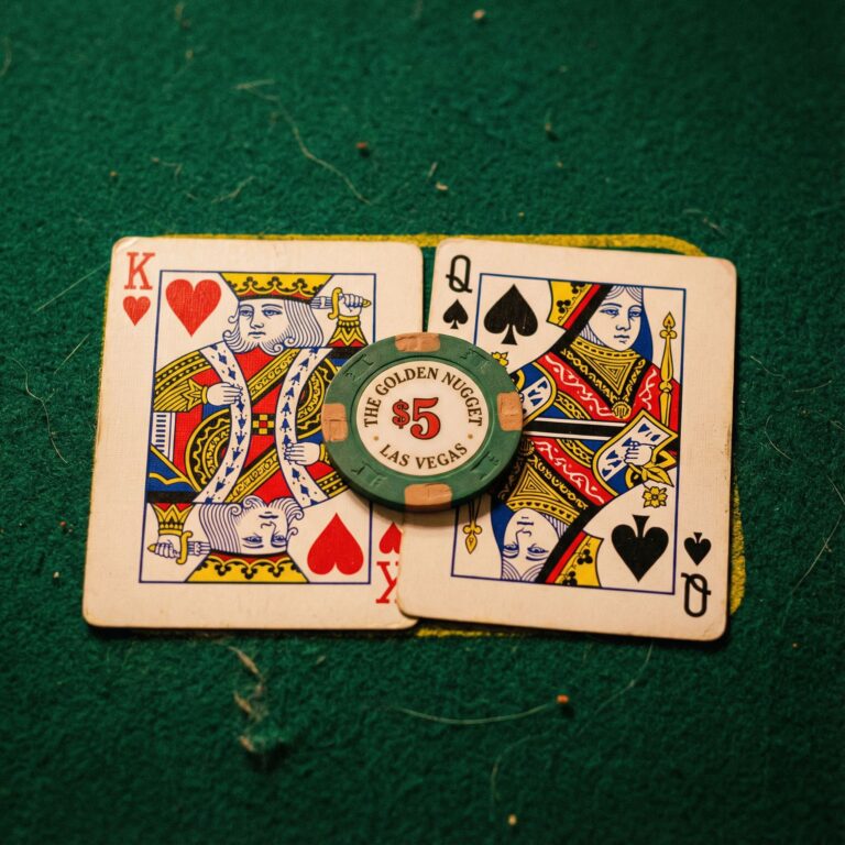 초록색 펠트 카지노 테이블 위에 나란히 놓인 킹과 퀸 카드, 그 위에 포커 칩 하나가 얹혀 있는 모습이다.