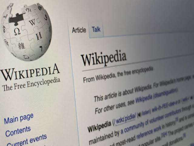 A close-up shot of a digital screen displaying the Wikipedia website, featuring the puzzle globe logo and the main article header reading "Wikipedia: From Wikipedia, the free encyclopedia".